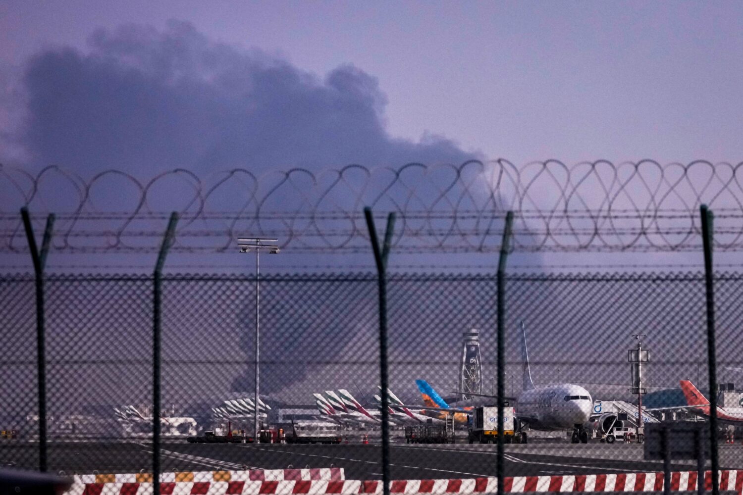 Planes are parked at Dubai International Airport as smoke rises in the background after a drone str...