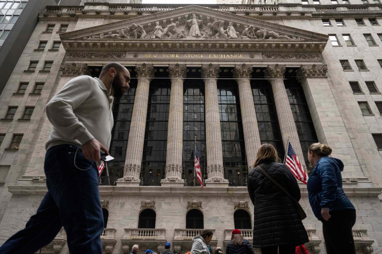 People walk past the New York Stock Exchange, Friday, March 27, 2026, in New York. (AP Photo/Yuki I...