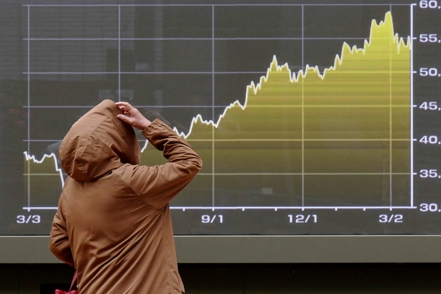 A person looks at an electronic stock board showing Japan's Nikkei index chart at a securities firm...