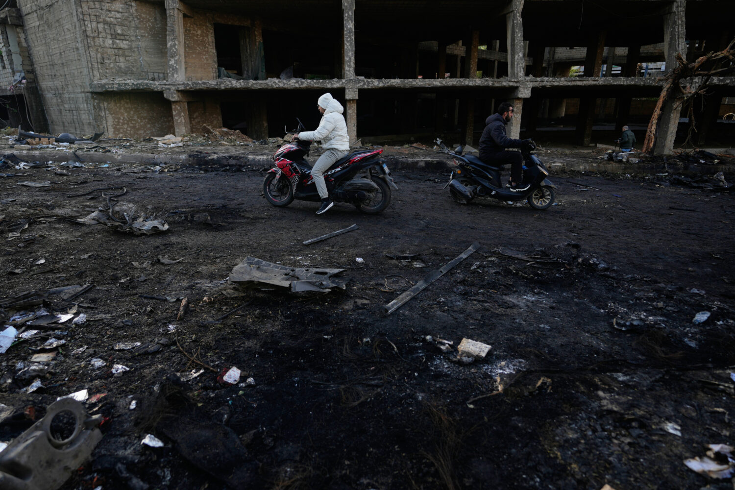 Two men ride scooters past charred debris at the site of an Israeli strike in Beirut, Lebanon, Wedn...