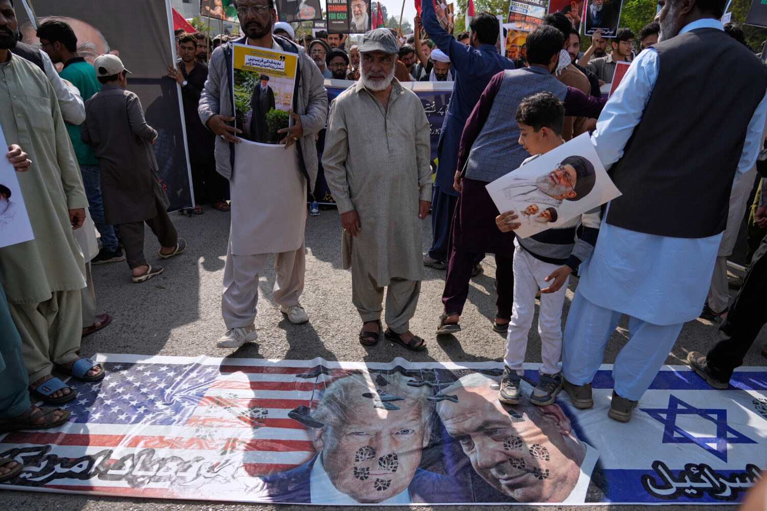 Shiite Muslims walk over the representation of U.S. and Israeli flags with pictures of President Do...