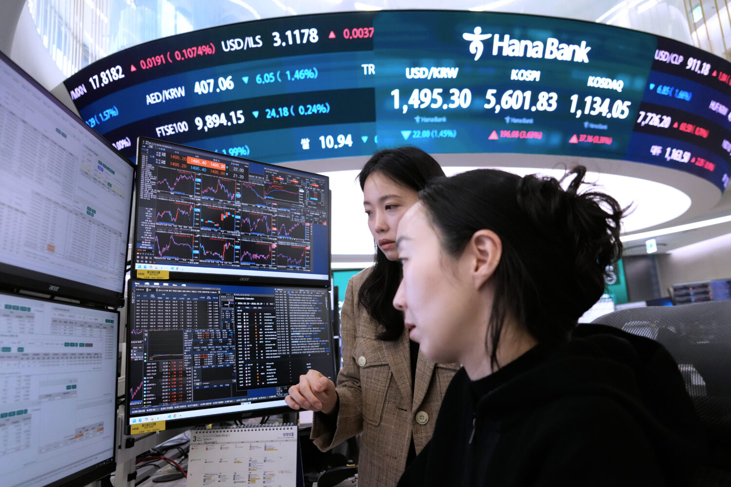 Currency traders watch monitors near a screen showing the Korea Composite Stock Price Index (KOSPI)...