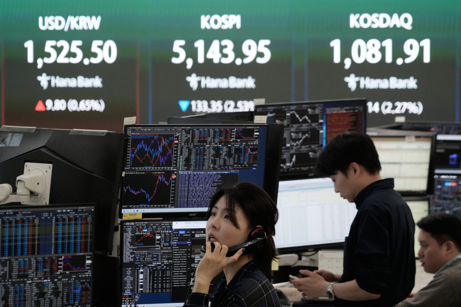 A currency trader talks on the phone near a screen showing the Korea Composite Stock Price Index (K...