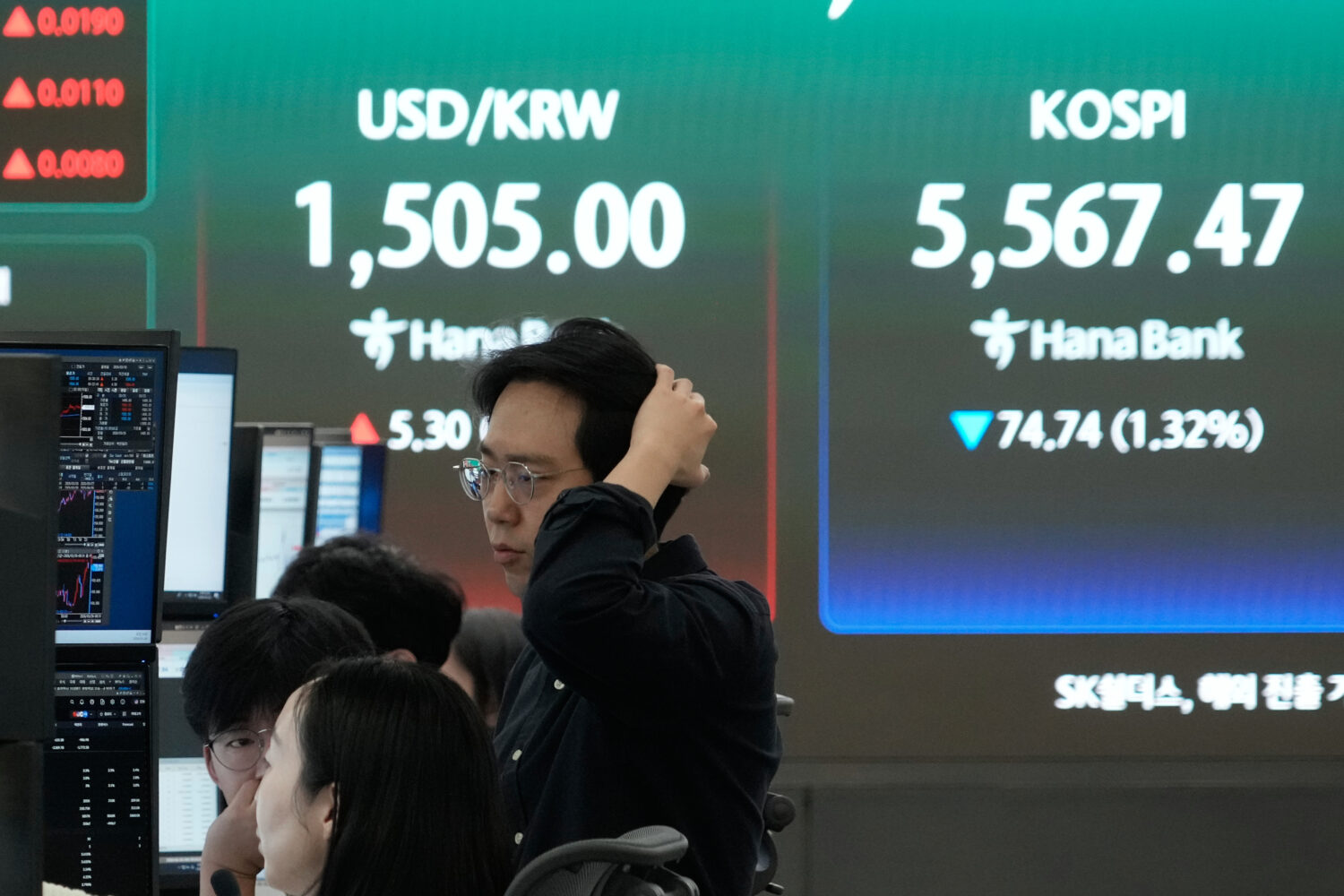 Currency traders watch monitors near a screen showing the Korea Composite Stock Price Index (KOSPI)...