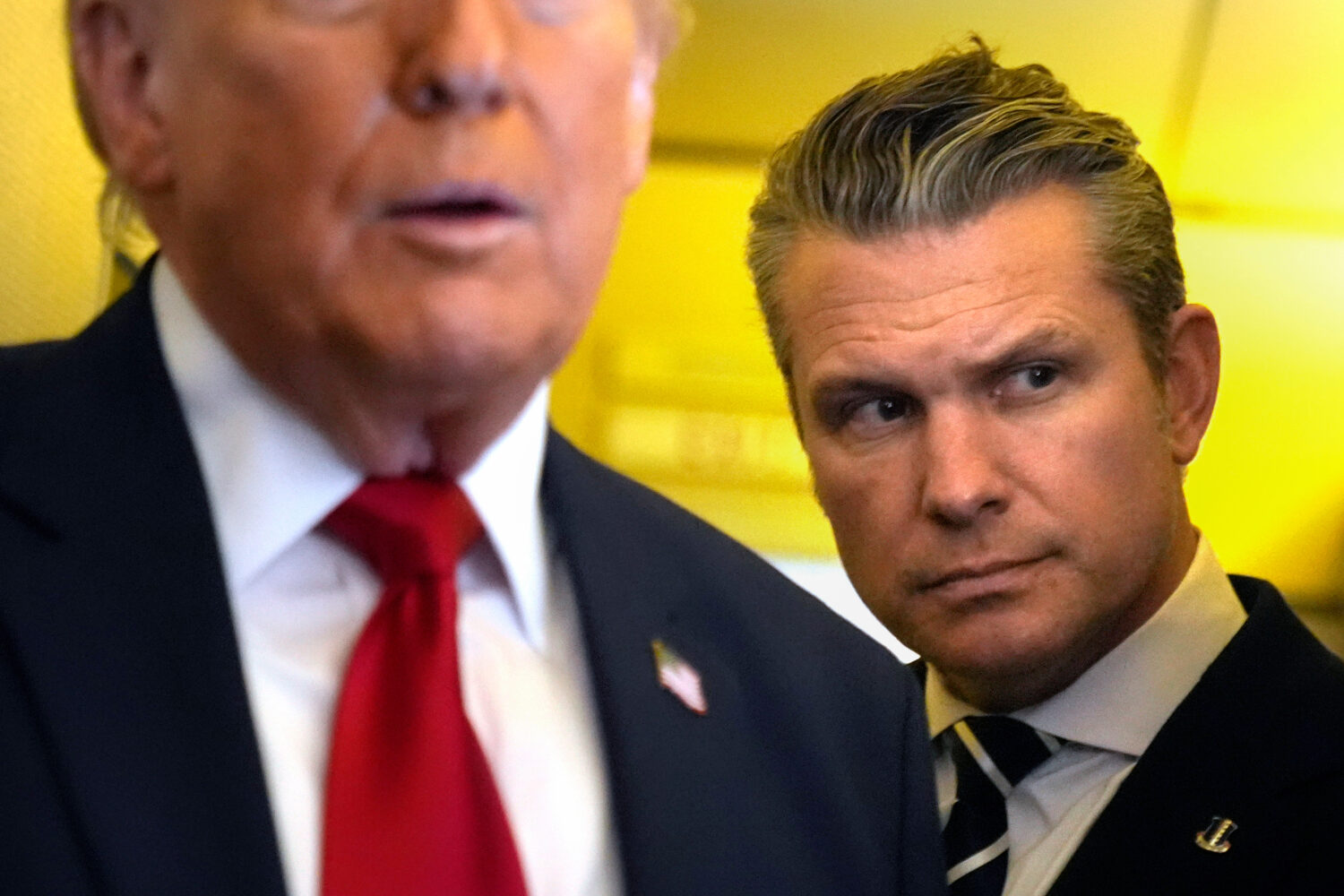 Defense Secretary Pete Hegseth listens as President Donald Trump speaks to reporters while travelin...