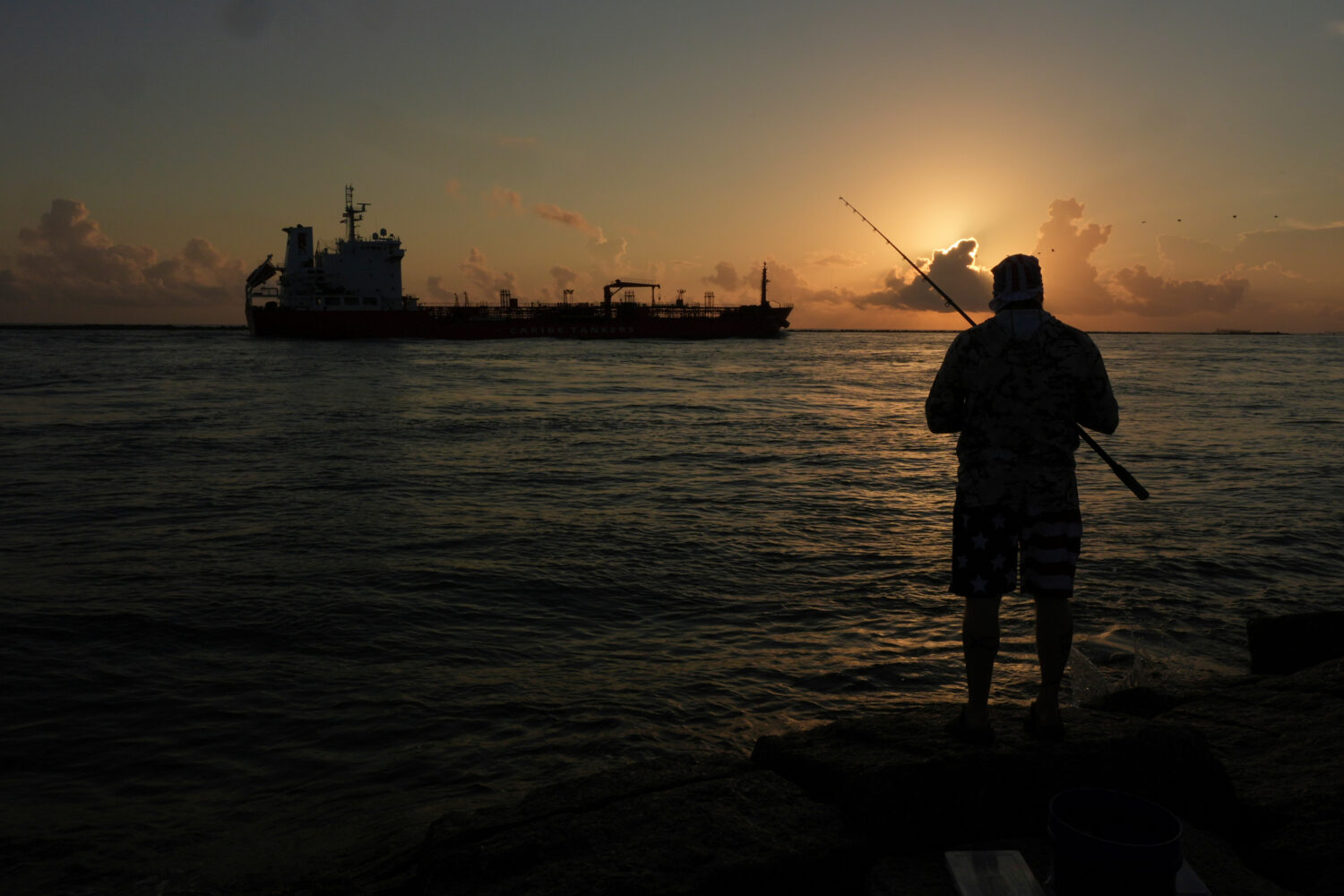 FILE - An oil tanker passes at sunrise while a man fishes in Port Aransas, Texas, Aug. 9, 2025. (AP...