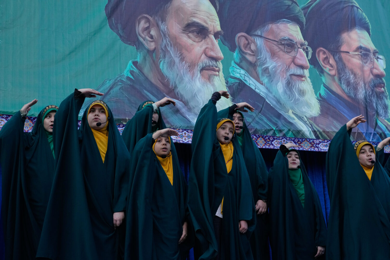 Girls sing a song as they show the movement of missiles with their hands next to the portraits of t...