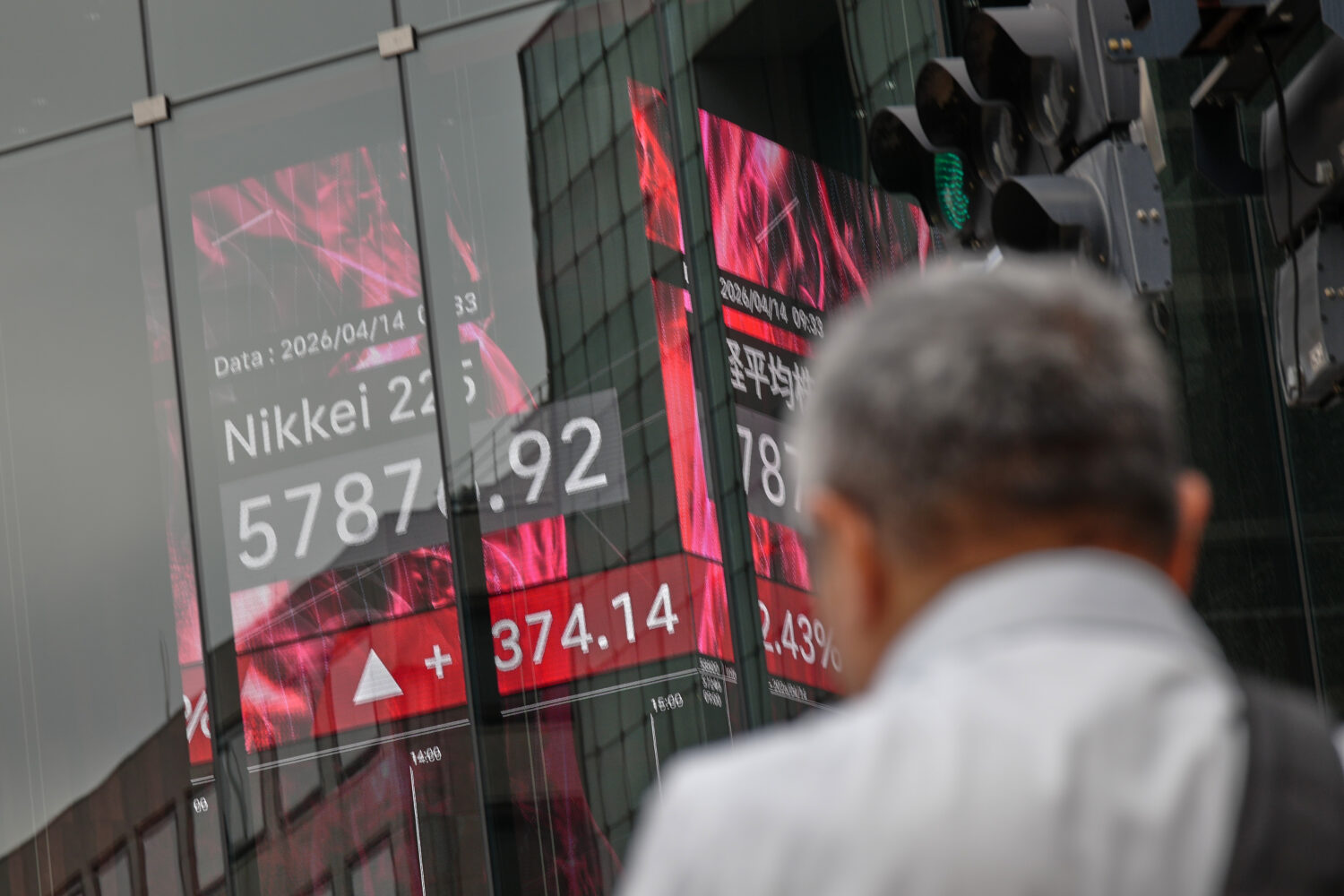 A person walks in front of an electronic stock board showing Japan's Nikkei index at a securities f...
