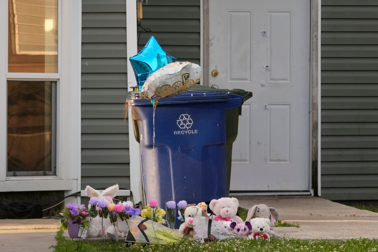 A makeshift memorial is growing on the front lawn of a home as the door in the background shows bul...
