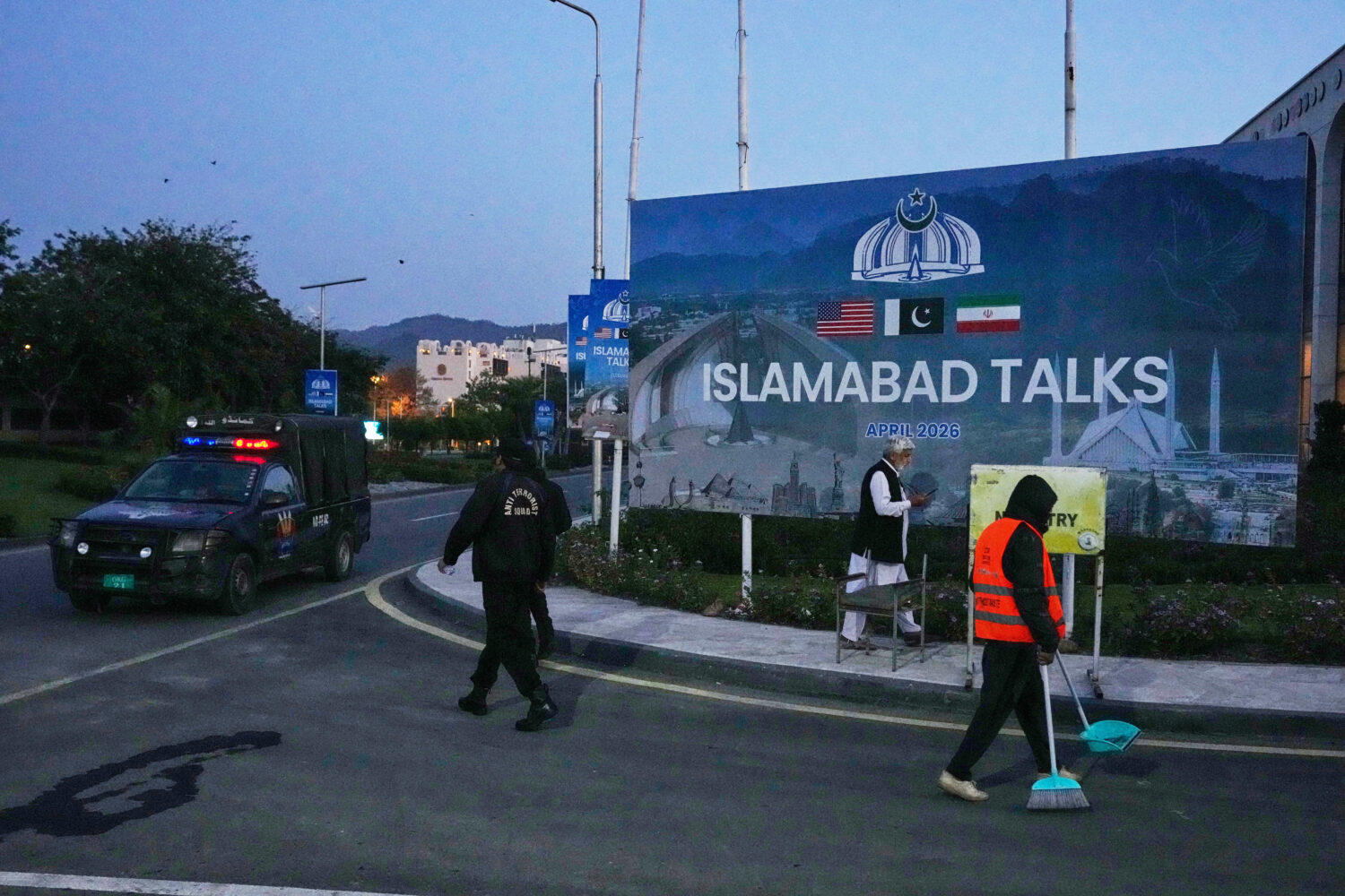 A worker cleans the street as police officers walks towards their vehicle outside a media center cl...
