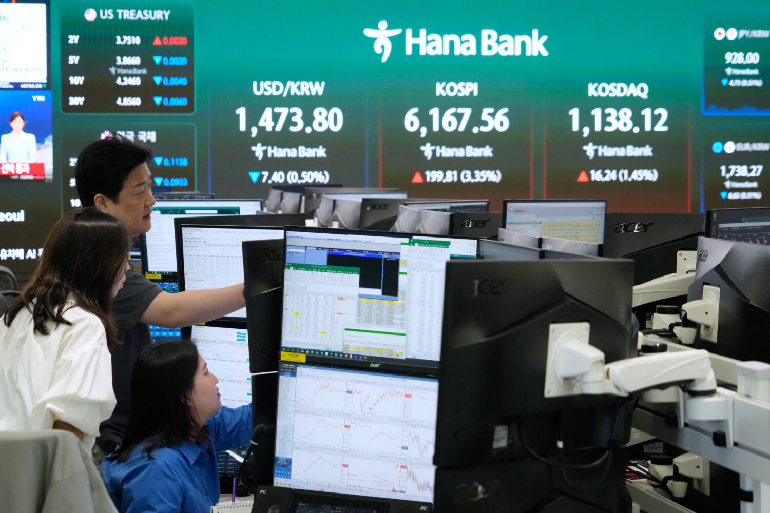 Currency traders watch monitors near a screen showing the Korea Composite Stock Price Index (KOSPI)...