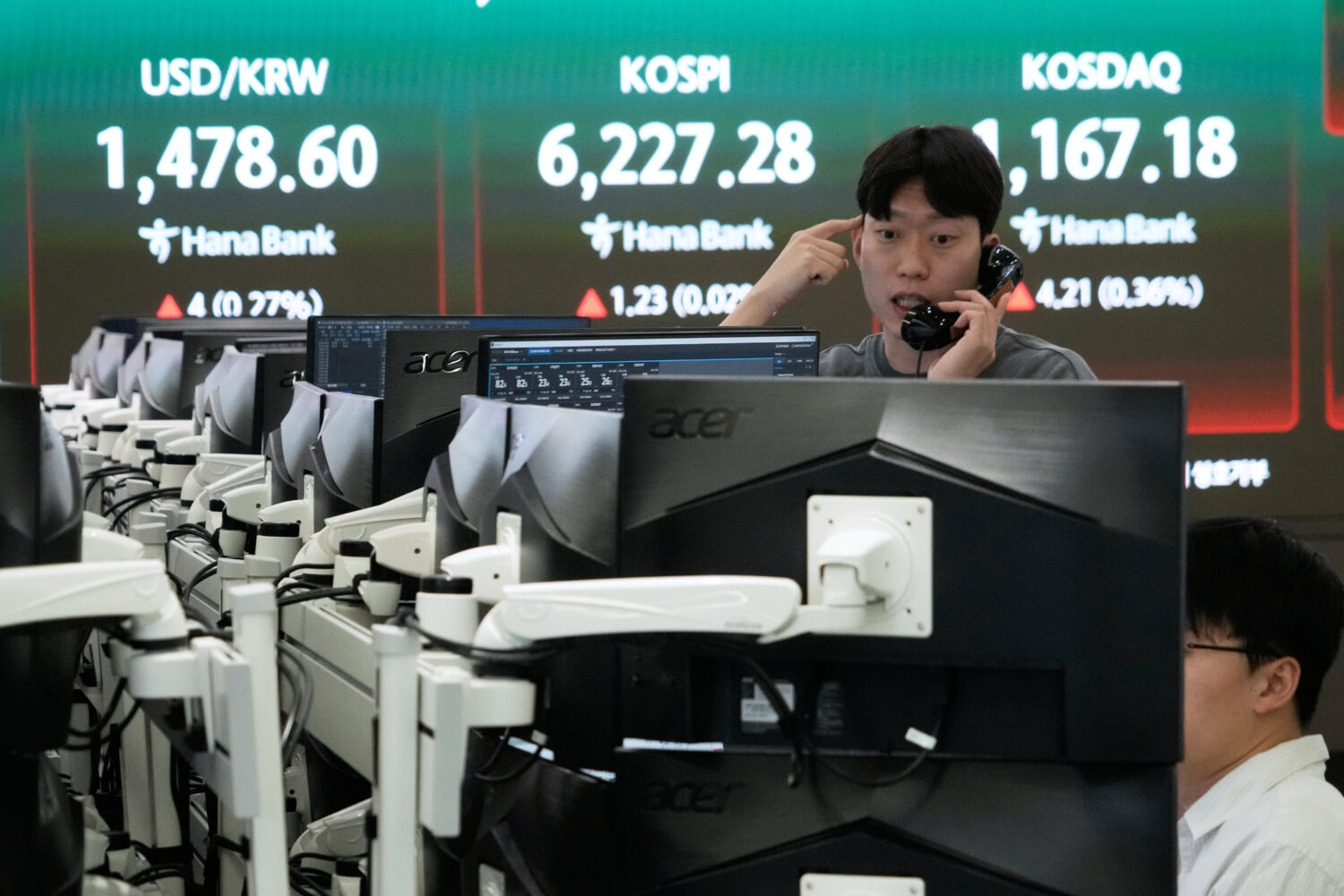 A currency trader talks on the phone near a screen showing the Korea Composite Stock Price Index (K...
