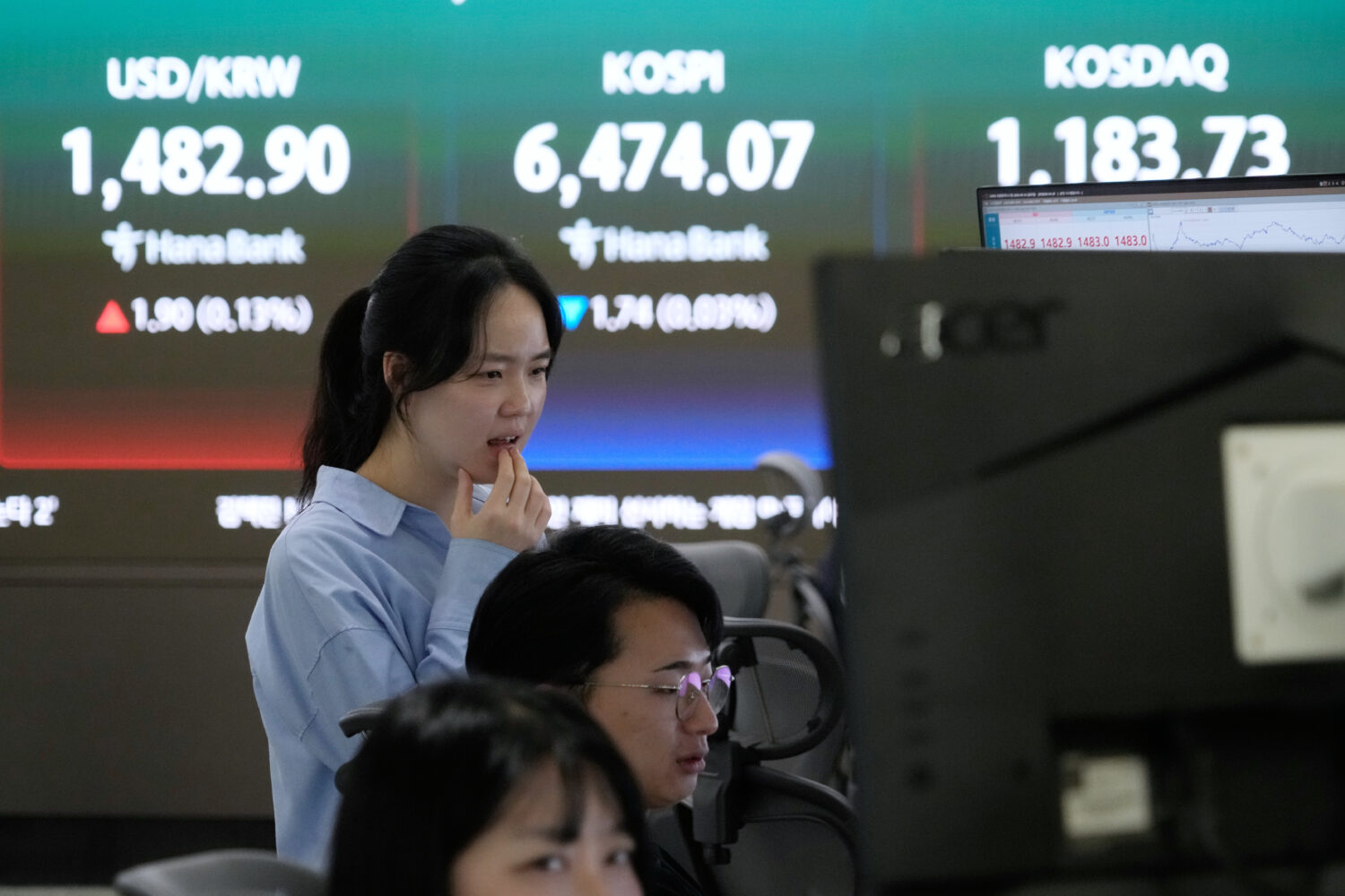 A currency trader watches monitors near a screen showing the Korea Composite Stock Price Index (KOS...
