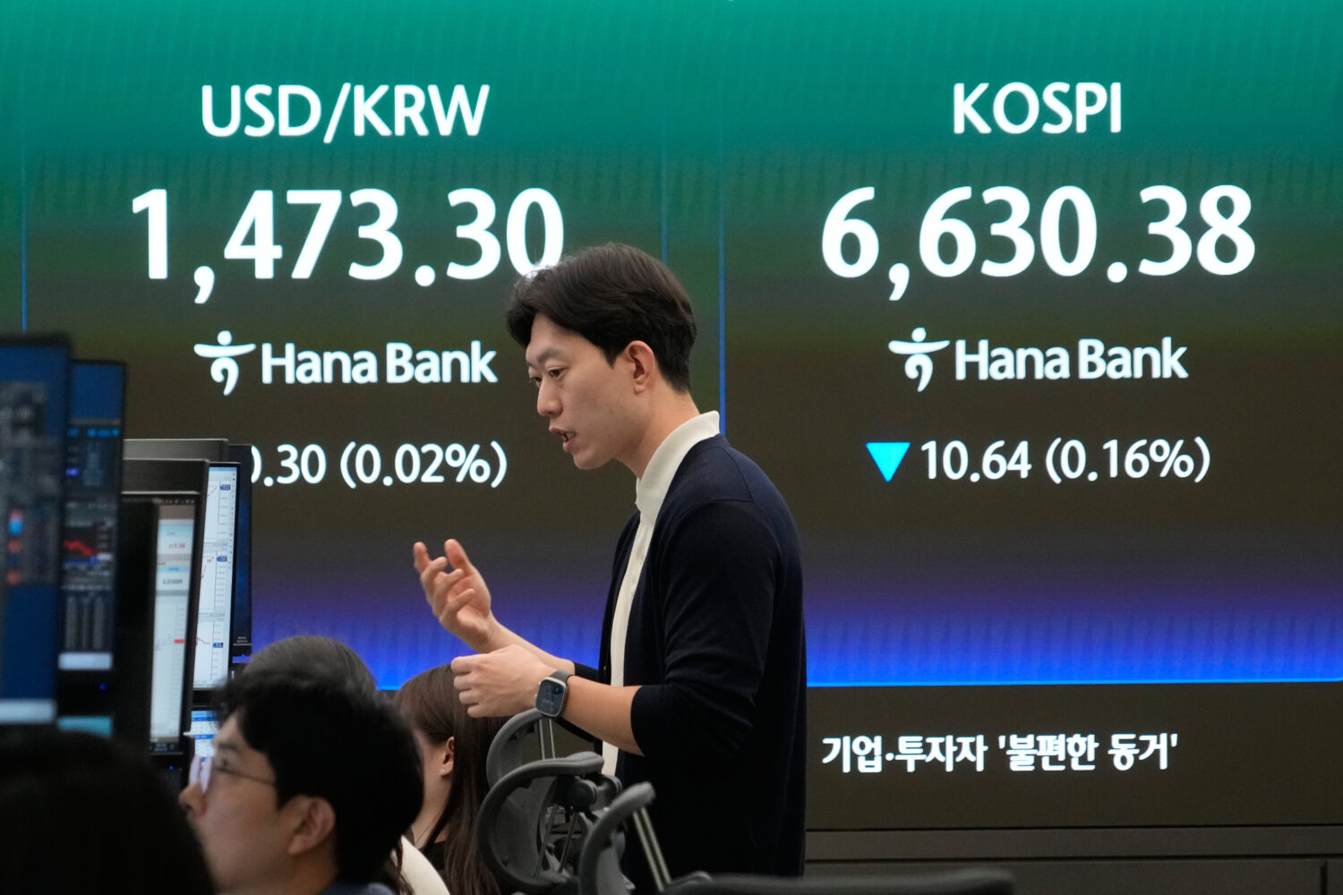 A currency trader reacts near a screen showing the Korea Composite Stock Price Index (KOSPI), right...