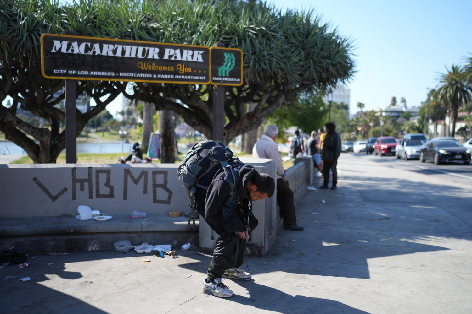 A man holding a pipe stands hunched over at MacArthur Park after federal authorities made arrests o...