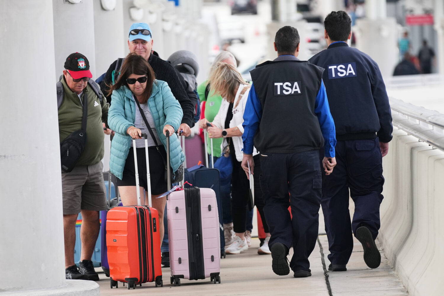 FILE - Travelers walk with their luggage past TSA agents at Fort Lauderdale-Hollywood International...