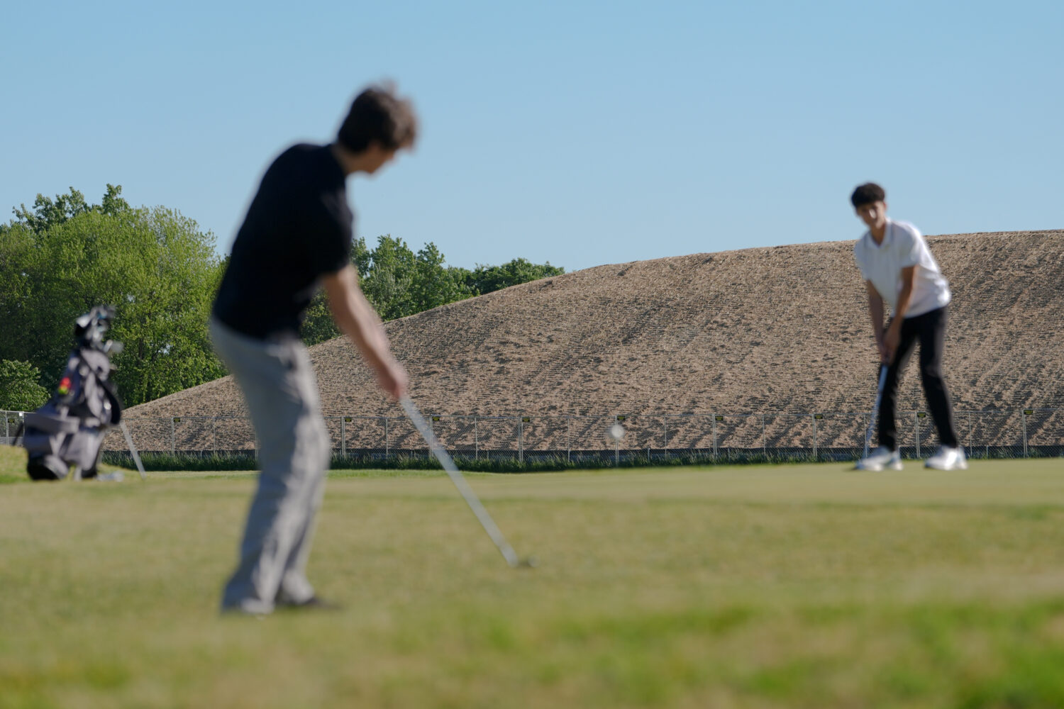 A pile of debris is seen in the background as Roman Sandoli, right, prepares to putt at the East Po...