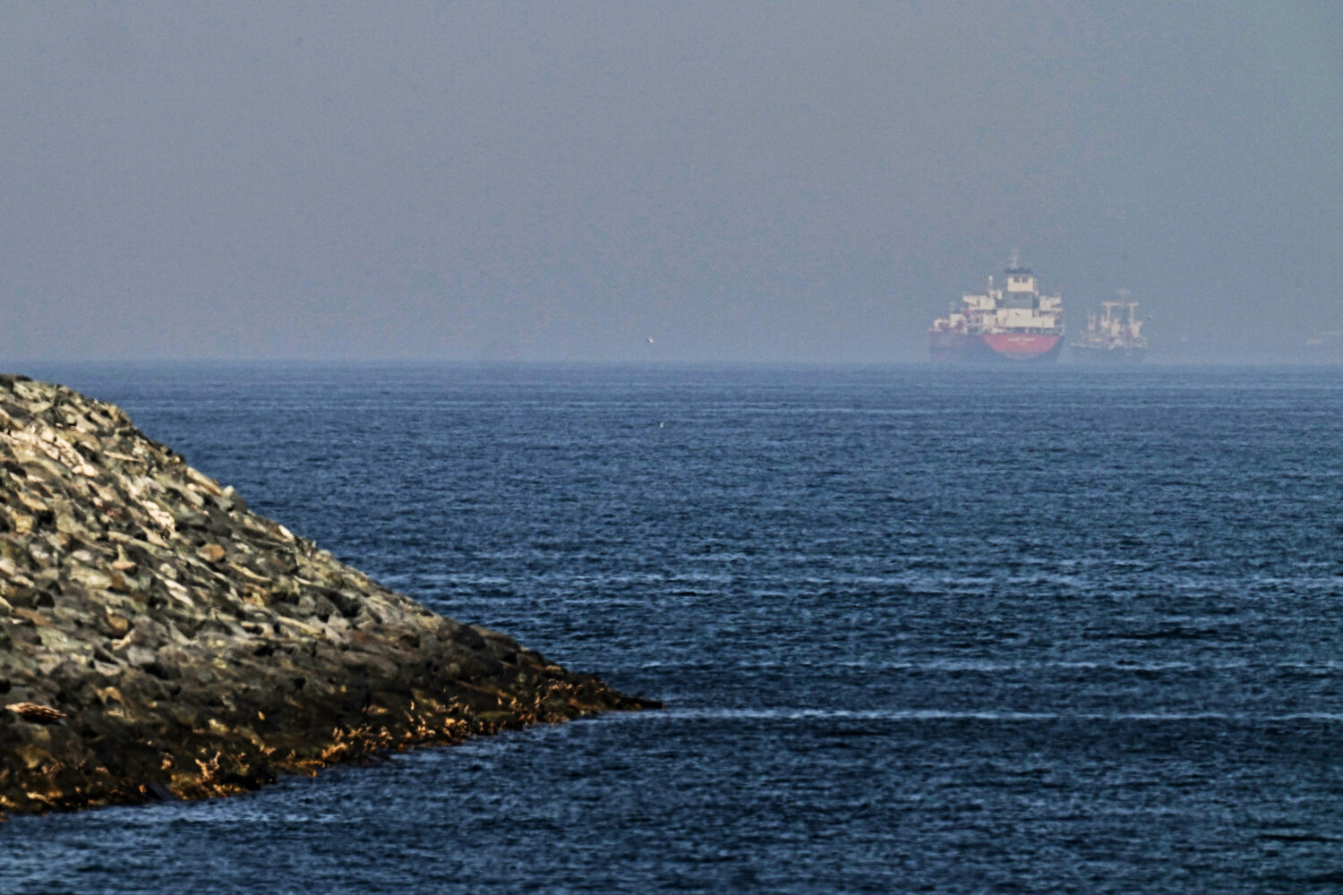 Cargo ships are seen at sea near the Strait of Hormuz, as viewed from a rocky shoreline near Khor F...