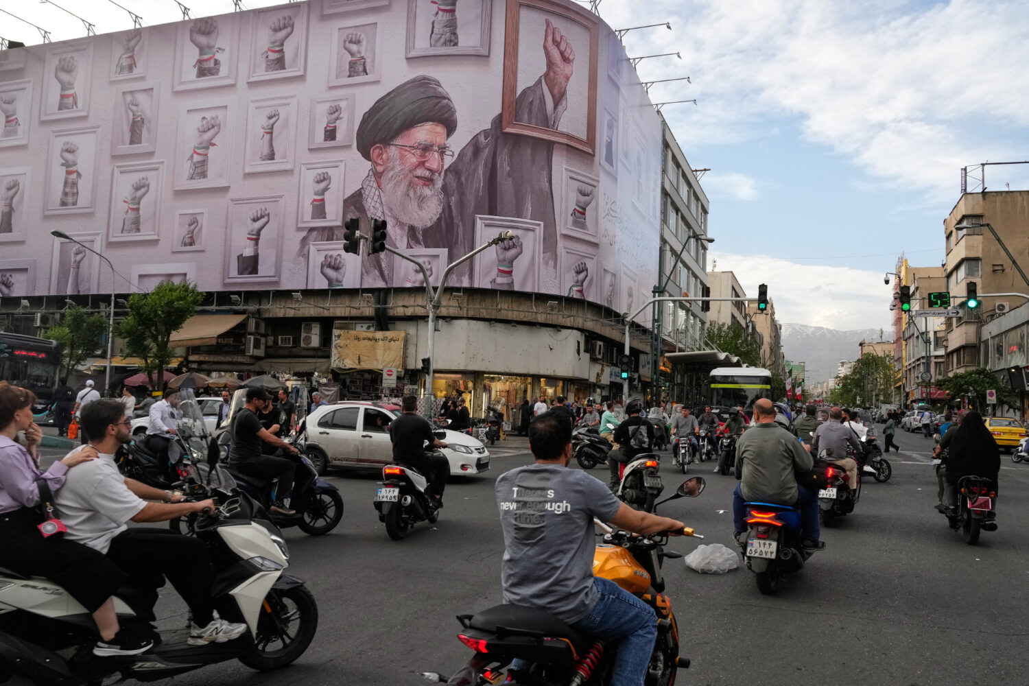 Motorbikes drive past a billboard with graphic showing the late Iranian Supreme Leader Ayatollah Al...
