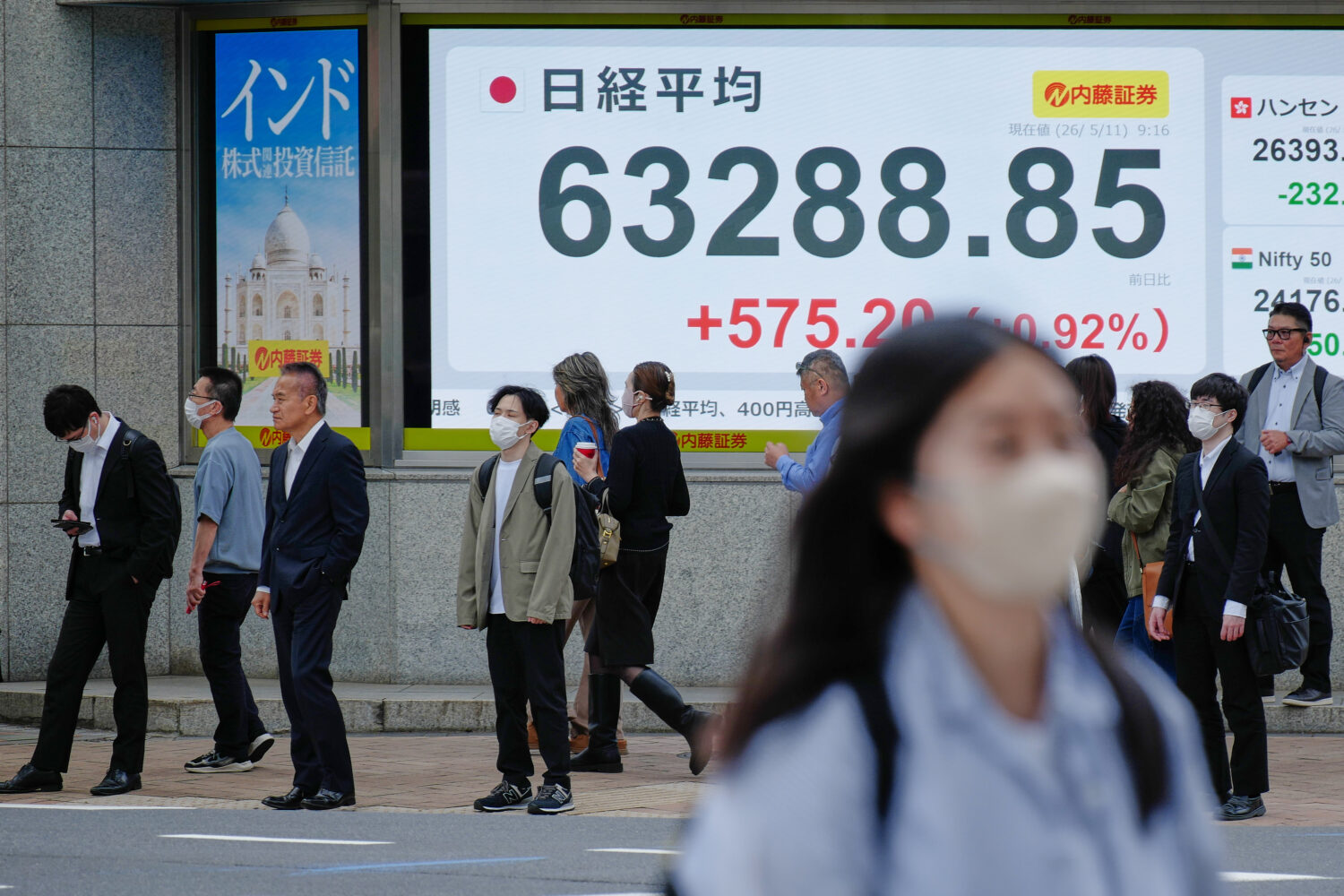 People stand in front of an electronic stock board showing Japan's Nikkei index at a securities fir...