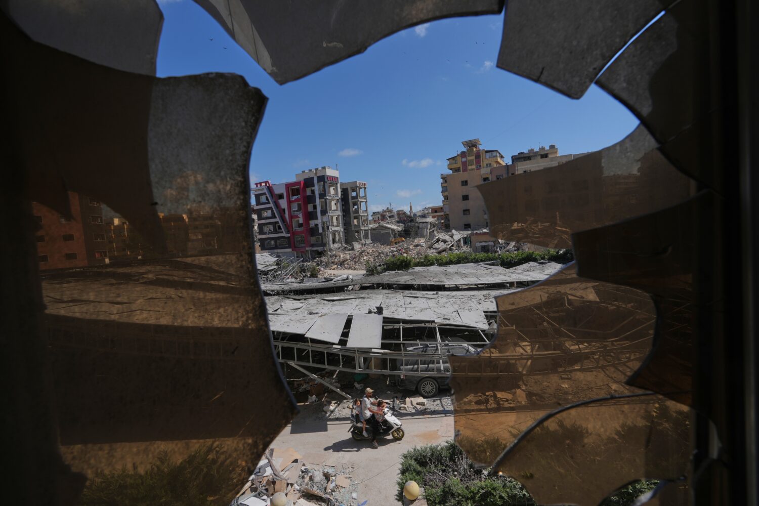 Buildings damaged by Israeli strikes are seen through shattered glass from the Jabal Amel Hospital ...