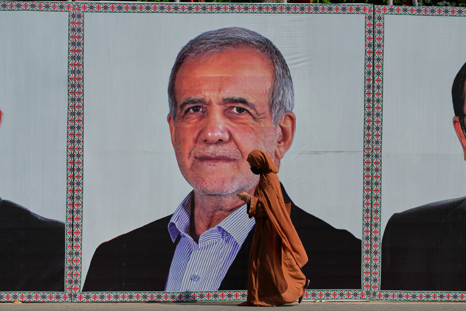 A woman walks past a welcoming billboard featuring Iranian President Masoud Pezeshkian along a road...