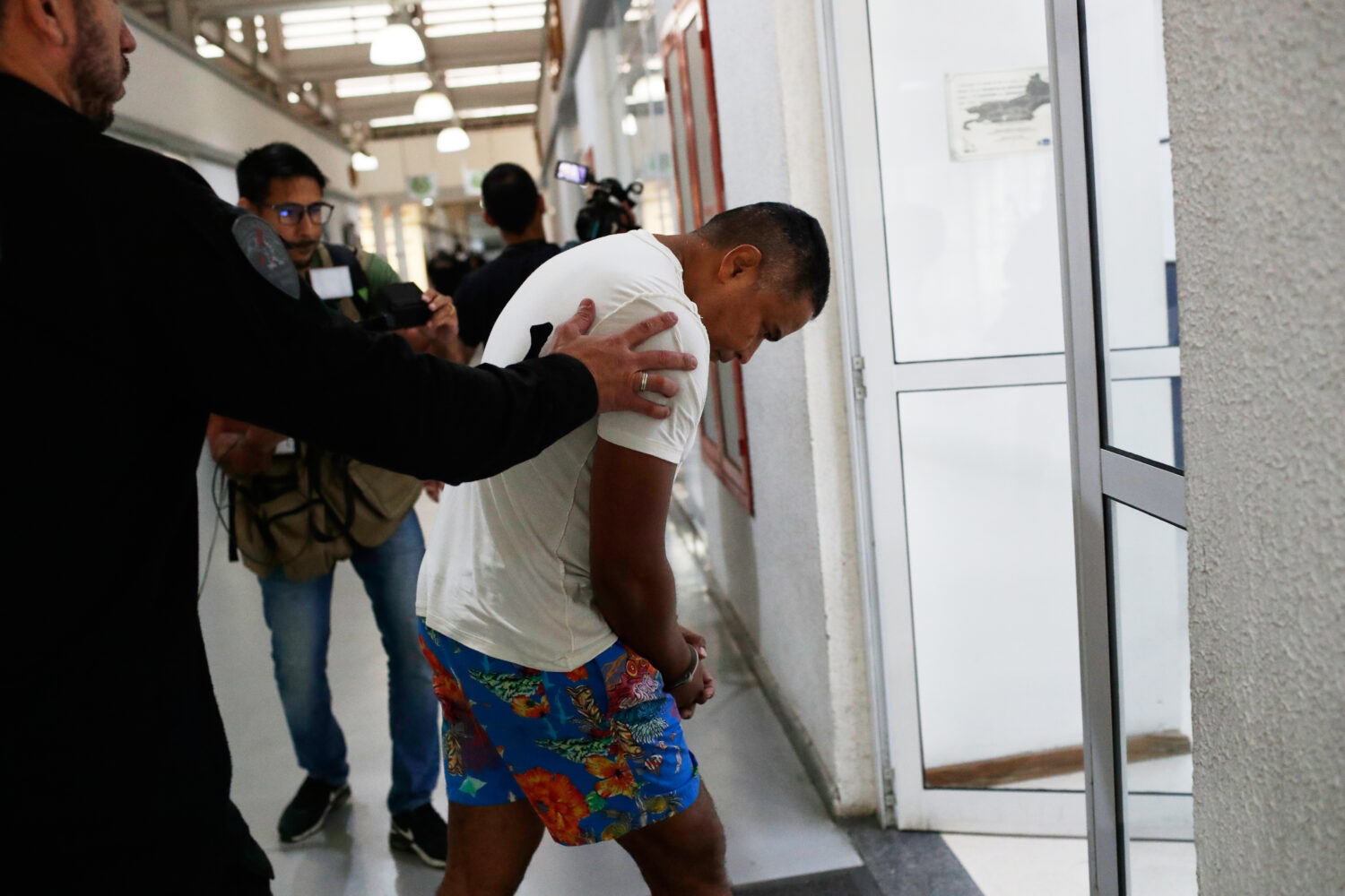 A suspected member of the criminal group Comando Vermelho, or Red Command, is lead in handcuffs by ...