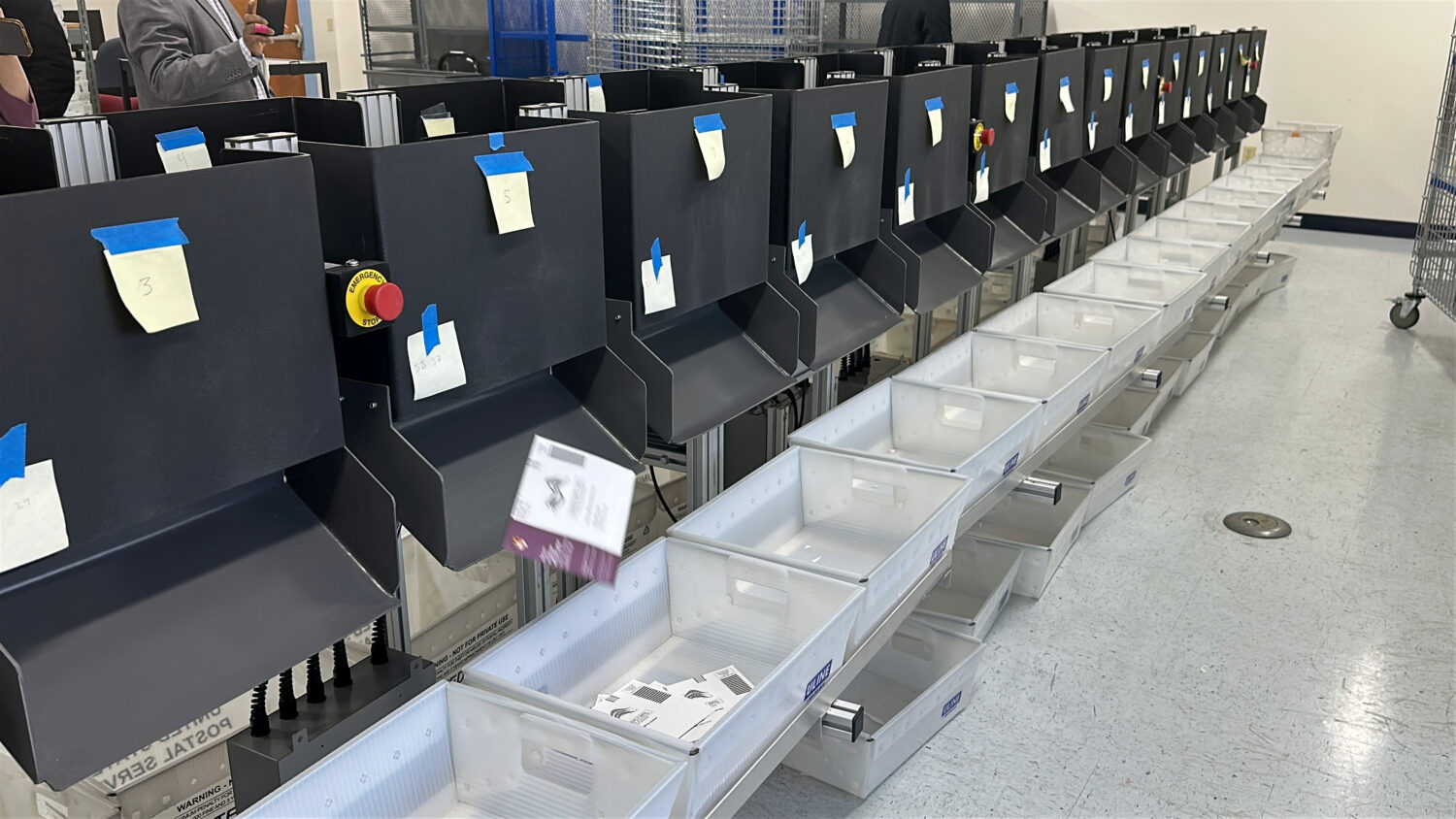 A sorting machine separates sample ballots into bins during a demonstration of voting equipment at ...