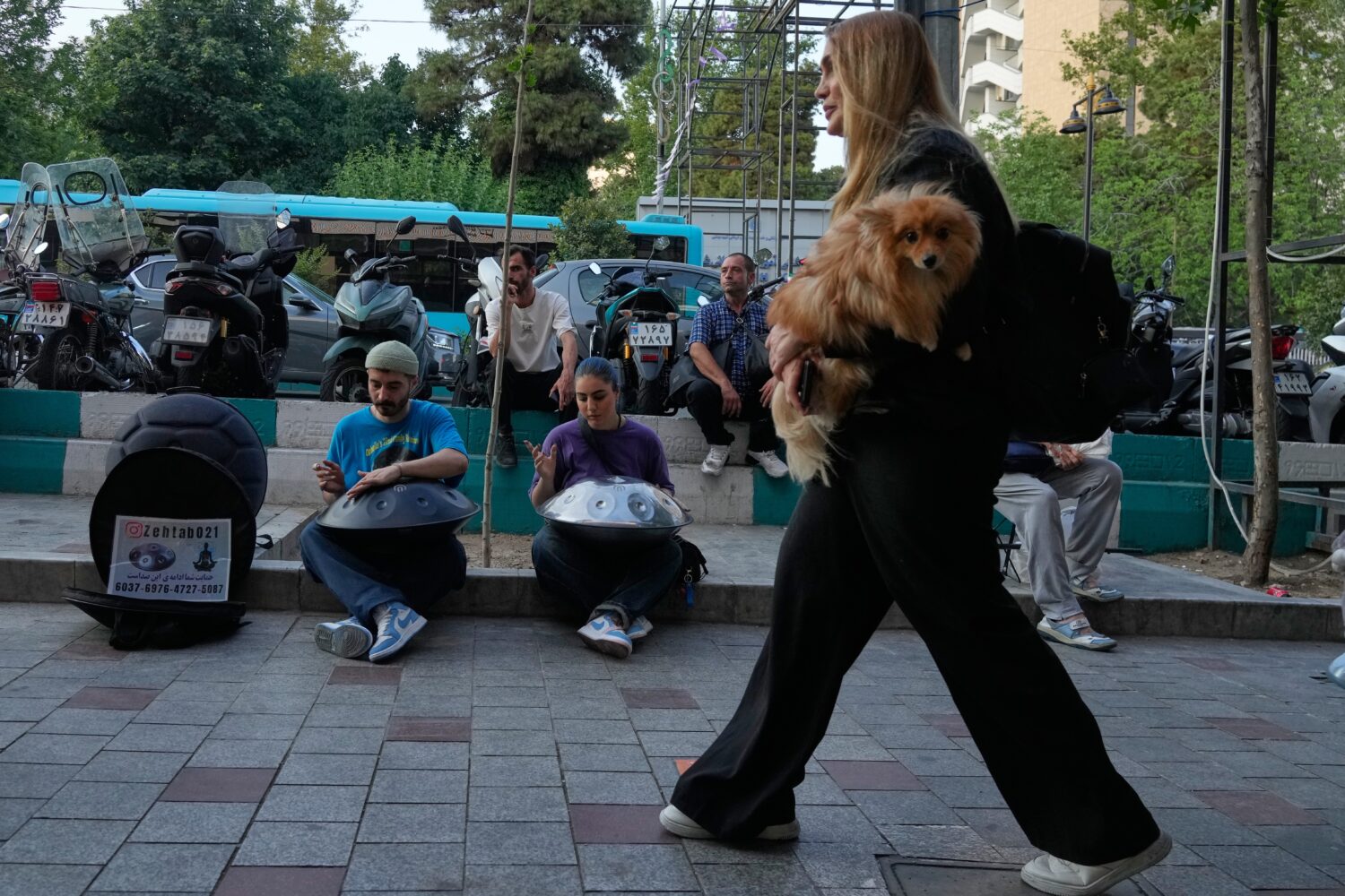 Street musicians play music as a woman carries a dog on a sidewalk in northern Tehran, Wednesday, J...