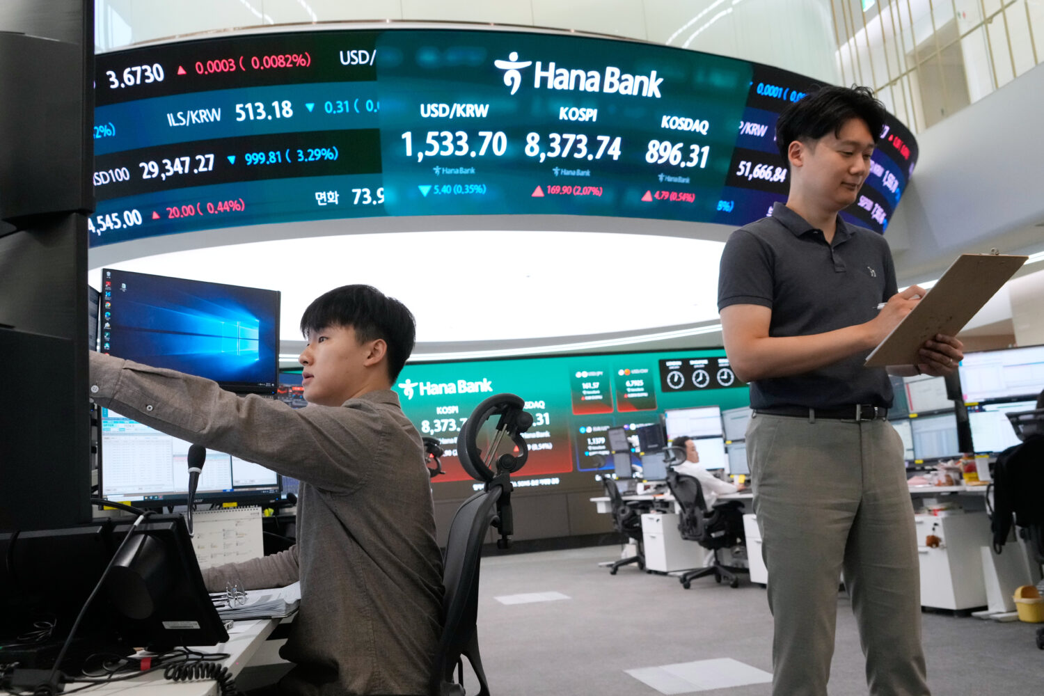 Currency traders work near a screen showing the Korea Composite Stock Price Index (KOSPI) and the f...