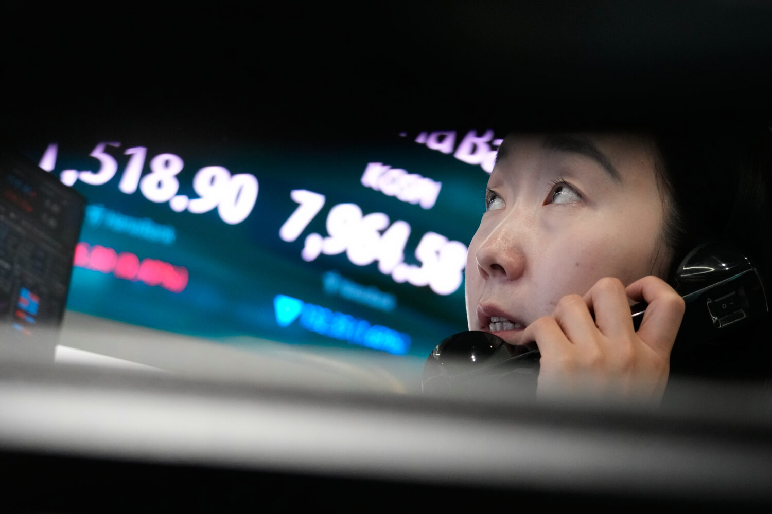 A currency trader talks on the phone near a screen showing the Korea Composite Stock Price Index (K...