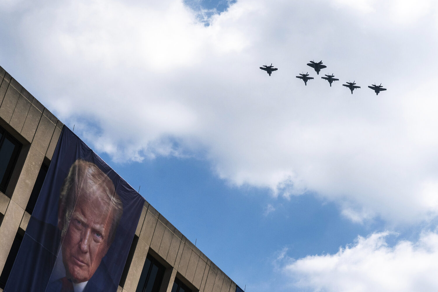 A flight of F-18s, F-35s and a F-22 fly past a picture of President Donald Trump hanging on the U.S...