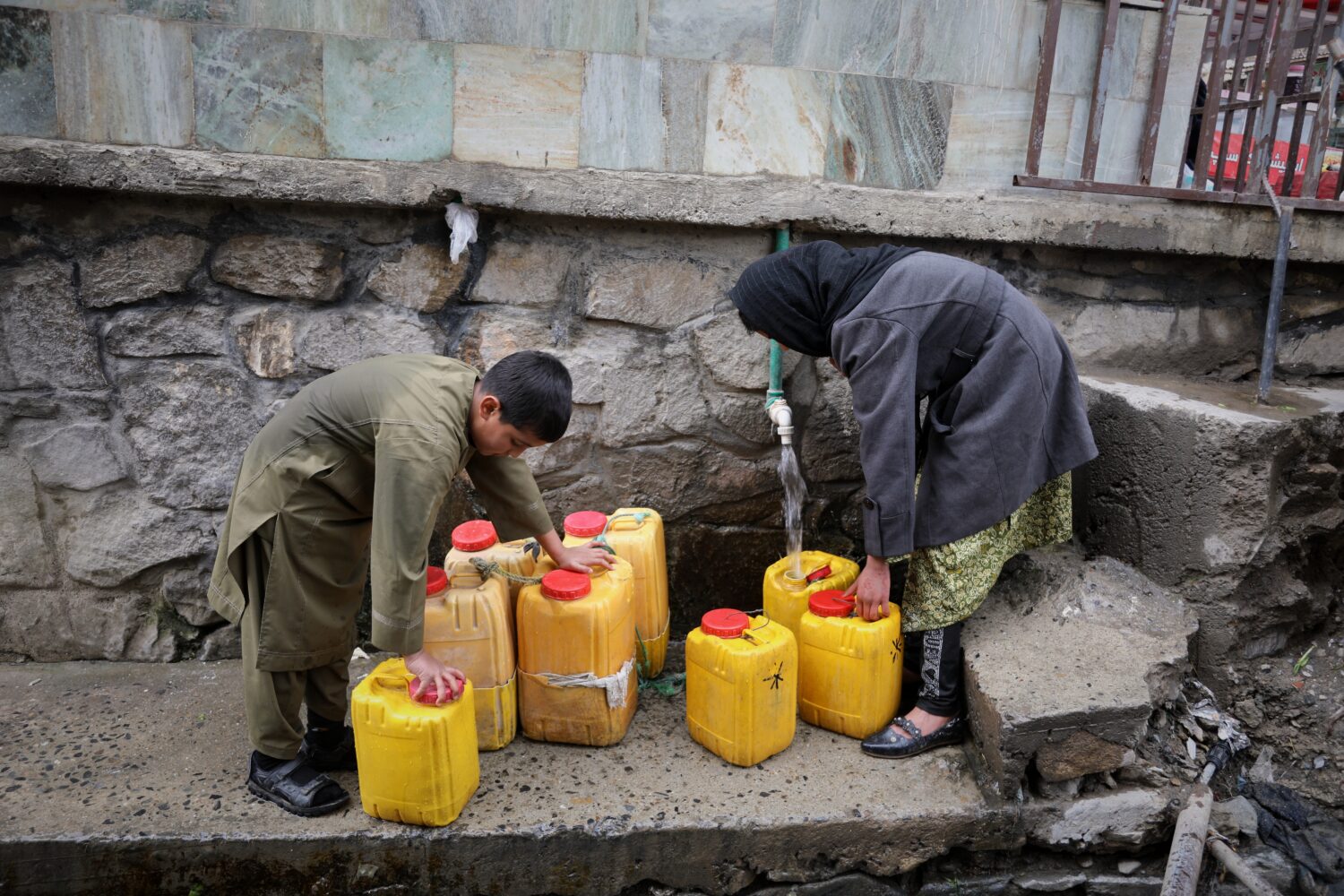 FILE - A boy and a girl collect water from a hose connected to a well at a mosque in Deh Mazang, Ka...