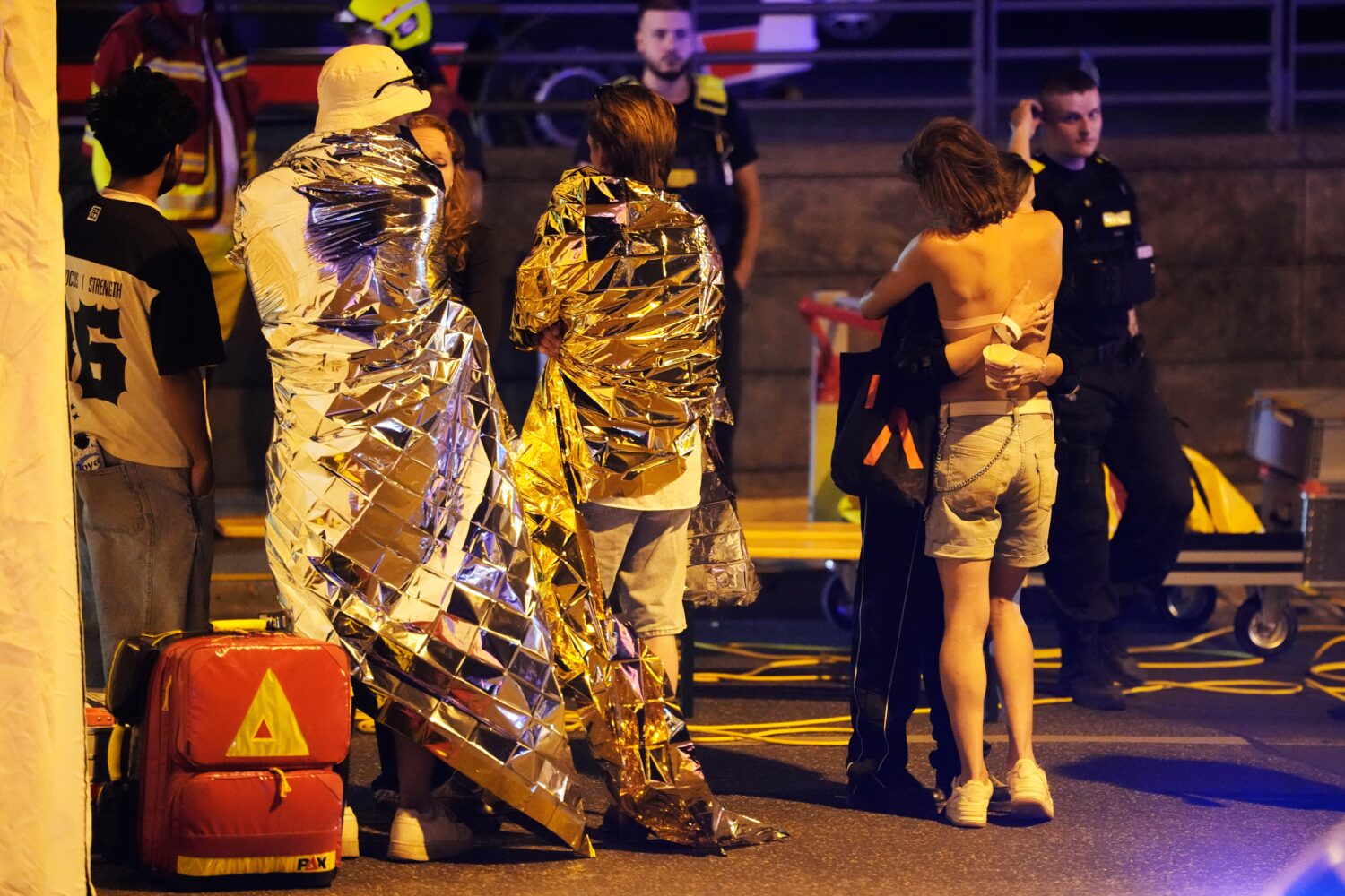 Two people embrace near others wearing thermal blankets as they stand near emergency personnel in B...