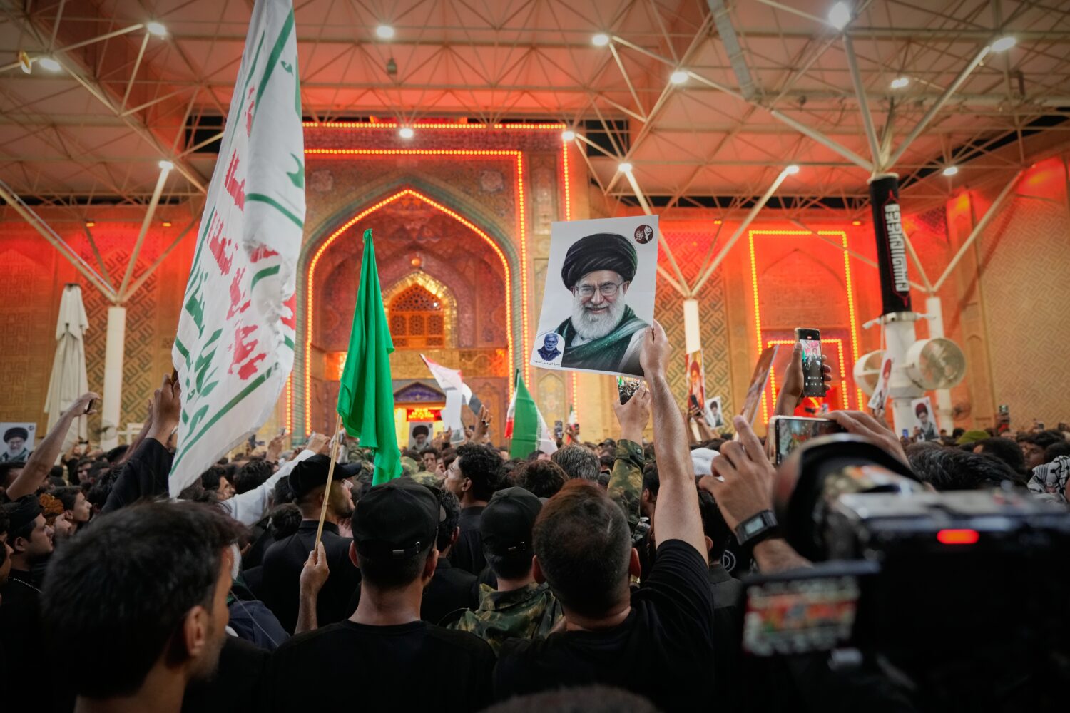 Mourners wave Shiite religious flags and a portrait of the late Iranian Supreme Leader Ayatollah Al...