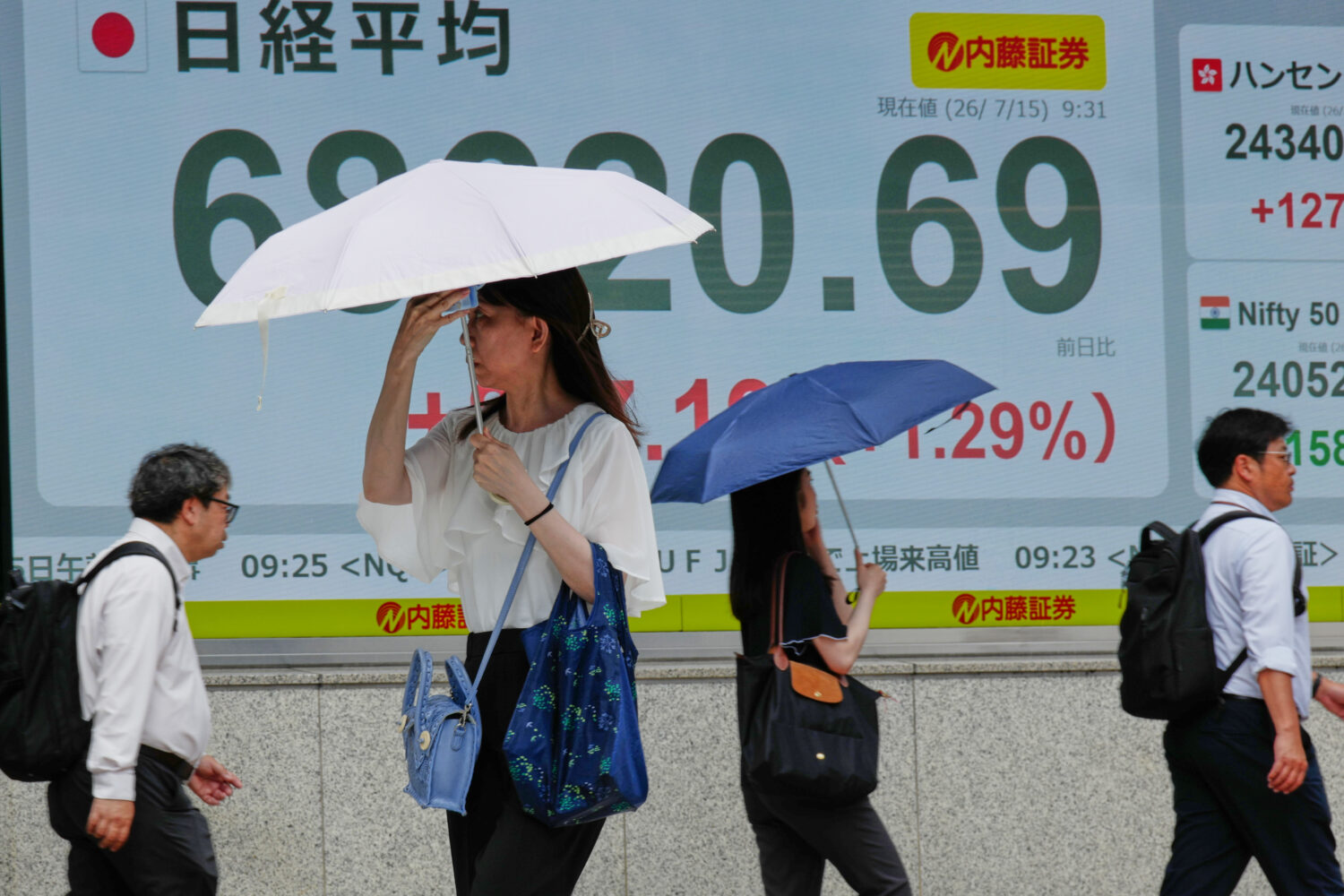 People walk in front of an electronic stock board showing Japan's Nikkei 225 index at a securities ...