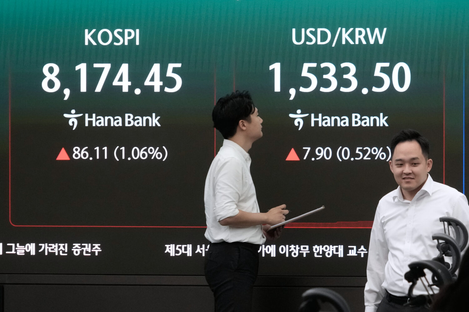 Currency traders pass by a screen showing the Korea Composite Stock Price Index (KOSPI) and the for...