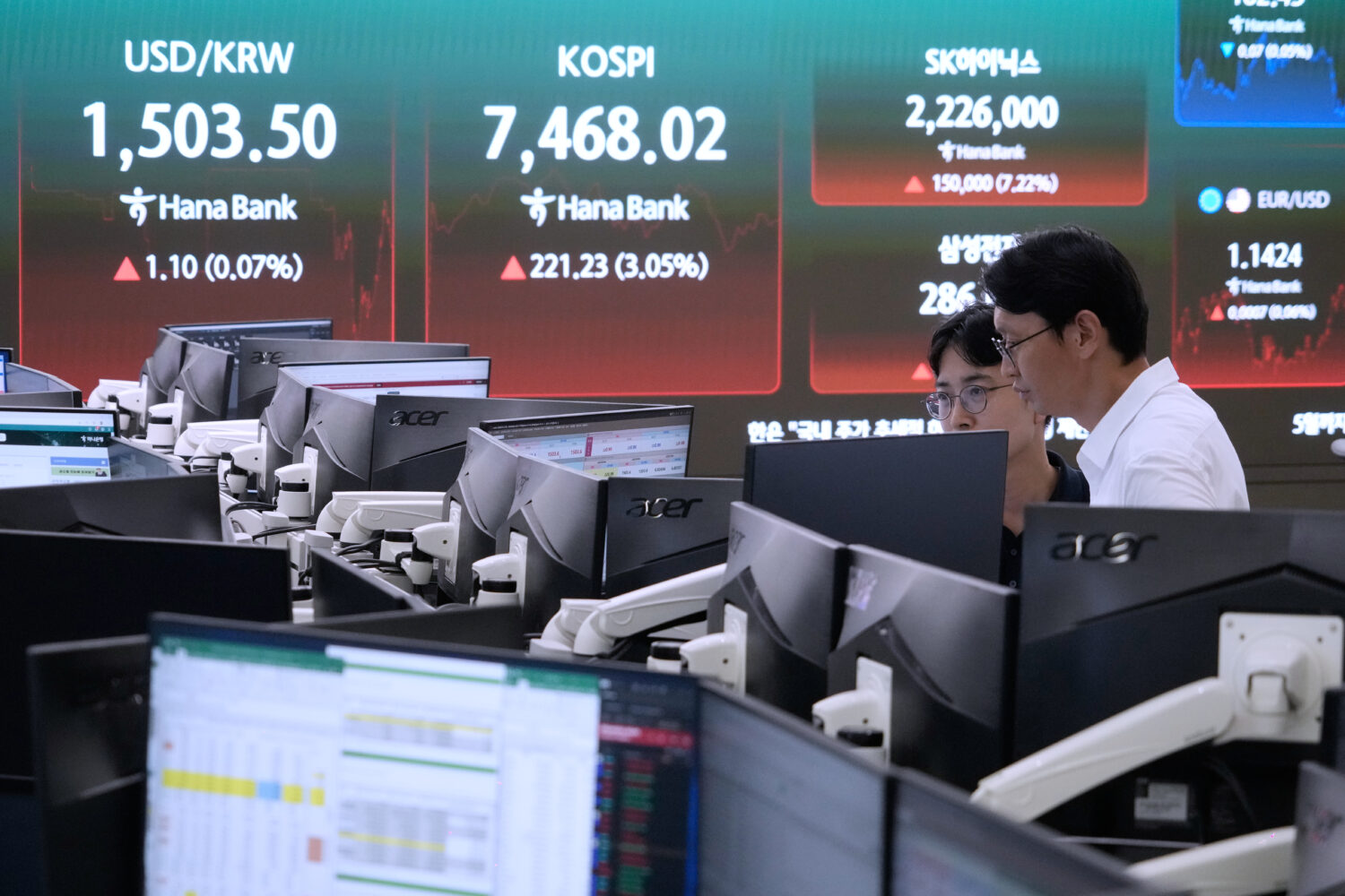 Currency traders watch monitors near a screen showing the Korea Composite Stock Price Index (KOSPI)...